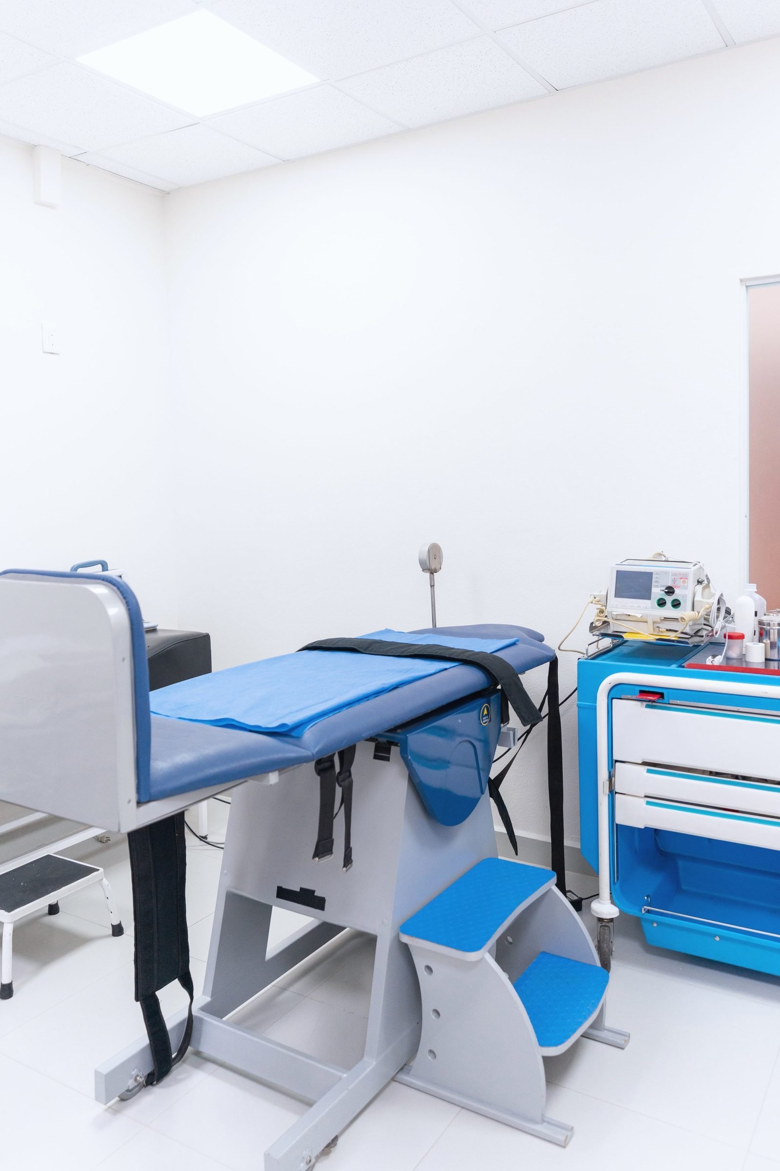 A clinical procedure room with an exam table and a supply cart